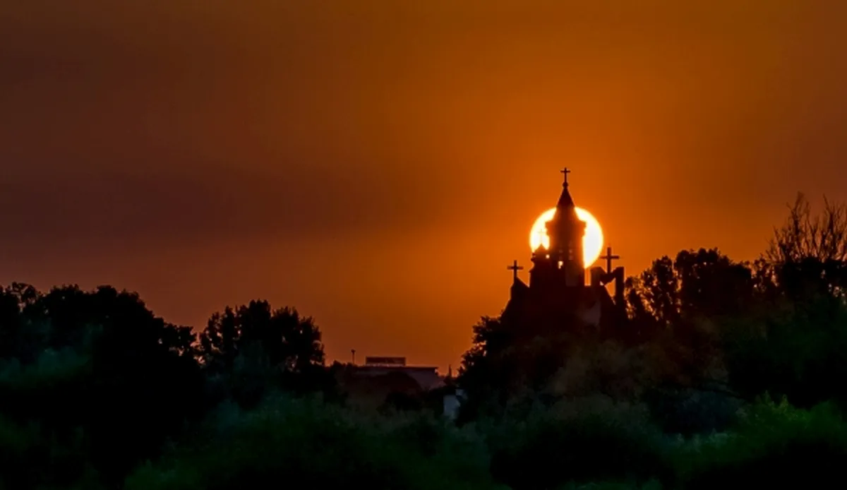 Church silhouette framed by a glowing orange sun at sunset